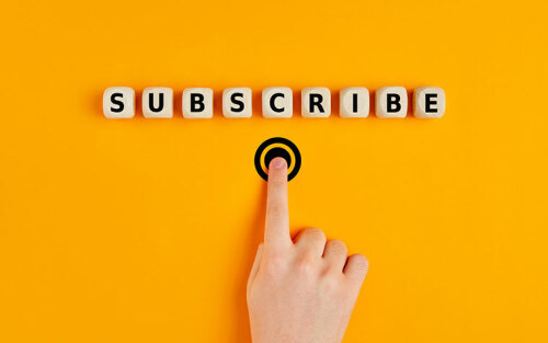 Hand pressing subscription button with the word subscribe written on wooden blocks