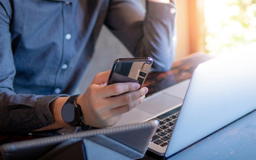 Man using his phone with laptop open in front of him